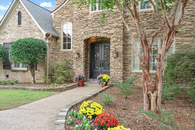 entrance to property with stone siding, french doors, and a shingled roof