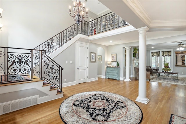 foyer entrance featuring crown molding, decorative columns, visible vents, wood finished floors, and ceiling fan with notable chandelier