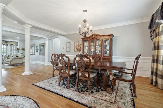 dining room featuring ornate columns, ornamental molding, light wood finished floors, and a wainscoted wall