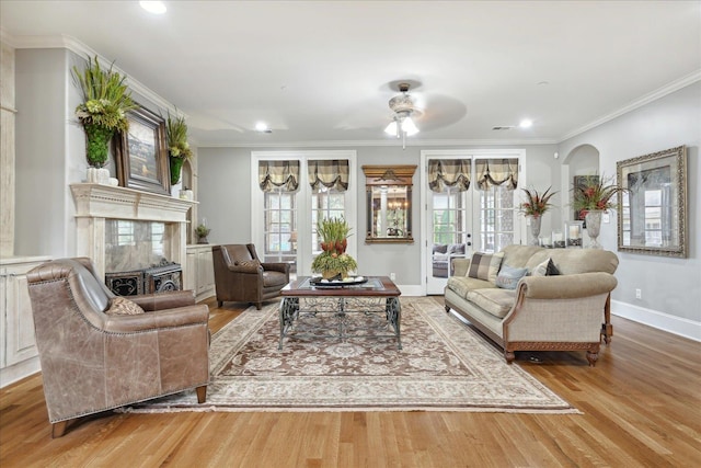 living room with arched walkways, a fireplace, wood finished floors, baseboards, and crown molding