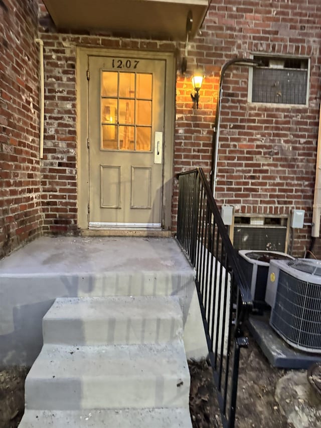 doorway to property featuring brick siding and central AC unit