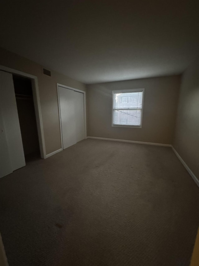 unfurnished bedroom with carpet, visible vents, baseboards, and two closets