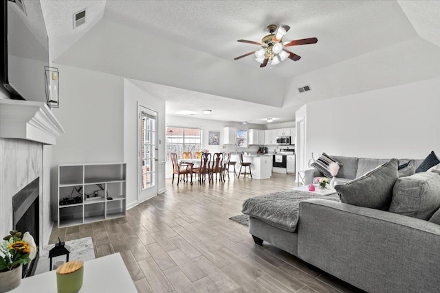 living area featuring a textured ceiling, light wood-type flooring, a fireplace with flush hearth, and visible vents