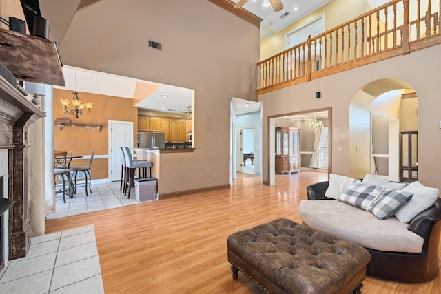 living area featuring ceiling fan with notable chandelier, light wood-style flooring, arched walkways, and visible vents