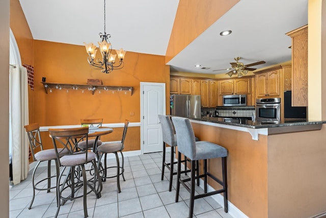 kitchen with decorative backsplash, appliances with stainless steel finishes, brown cabinets, a peninsula, and a kitchen bar