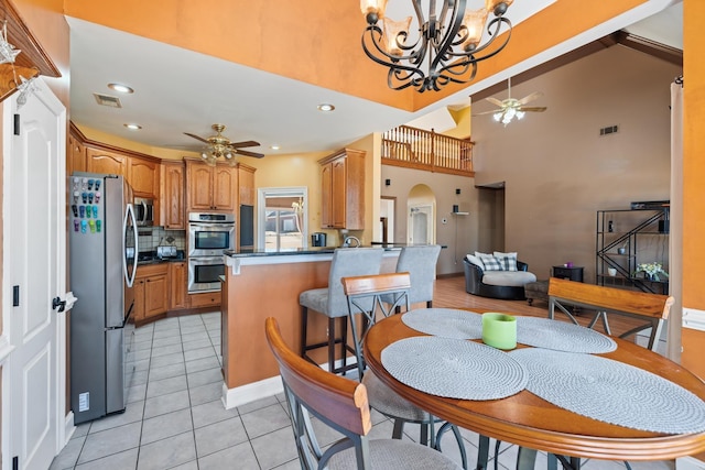 kitchen featuring dark countertops, a peninsula, stainless steel appliances, and ceiling fan with notable chandelier