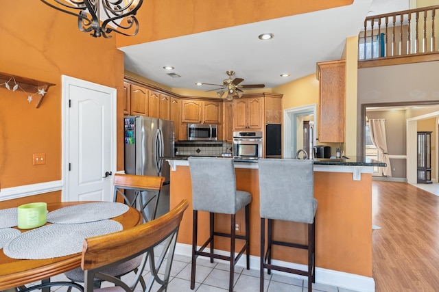 kitchen featuring a ceiling fan, appliances with stainless steel finishes, brown cabinets, a peninsula, and a kitchen bar