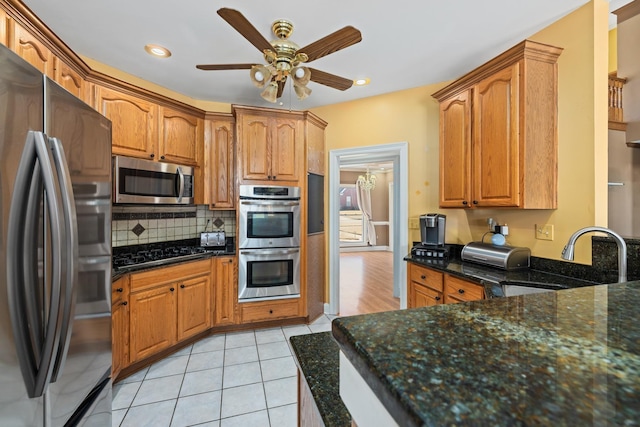 kitchen with light tile patterned floors, ceiling fan, appliances with stainless steel finishes, tasteful backsplash, and dark stone countertops