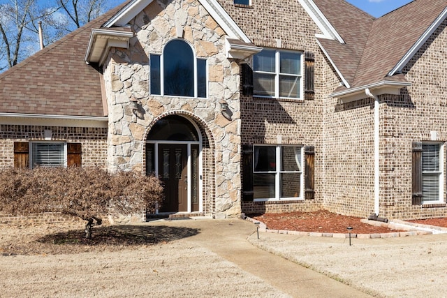 view of front of home with a shingled roof, stone siding, and brick siding