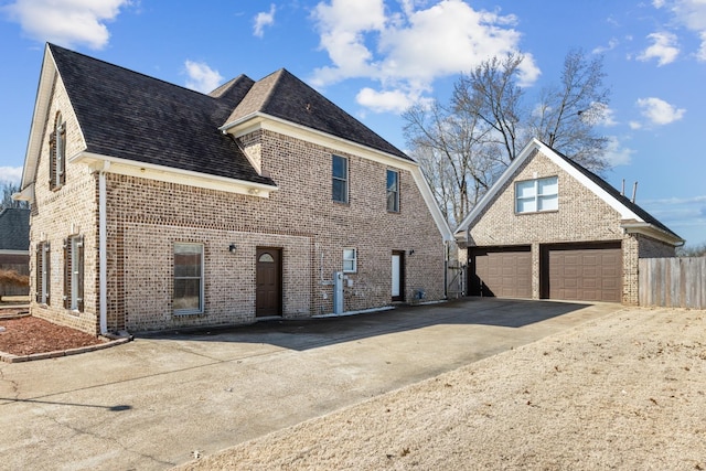 view of front of house with a shingled roof, brick siding, and fence