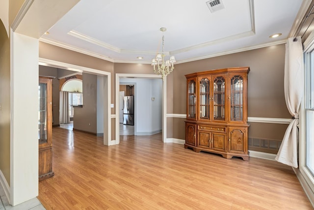 unfurnished dining area with arched walkways, a chandelier, visible vents, light wood finished floors, and a tray ceiling