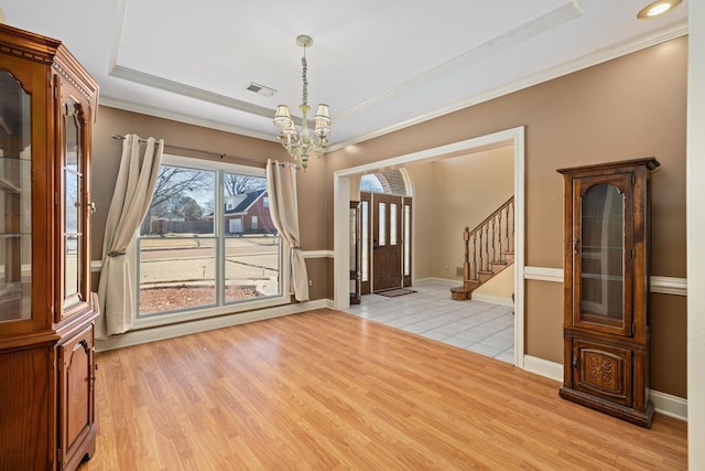 unfurnished dining area featuring a tray ceiling, crown molding, a notable chandelier, light wood-style flooring, and stairway