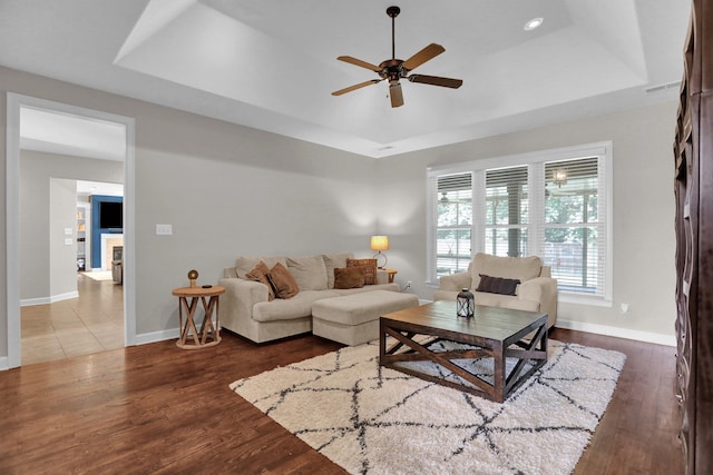 living area featuring a ceiling fan, baseboards, a tray ceiling, and wood finished floors