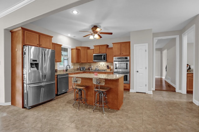 kitchen with stainless steel appliances, a kitchen island, a sink, backsplash, and light stone countertops