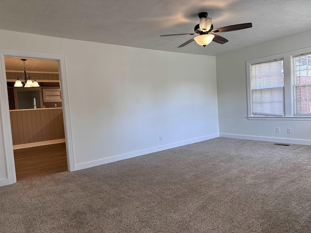 carpeted empty room with a textured ceiling, ceiling fan with notable chandelier, visible vents, and baseboards