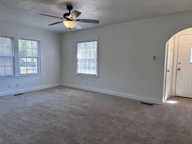 carpeted spare room featuring arched walkways, baseboards, visible vents, and a healthy amount of sunlight