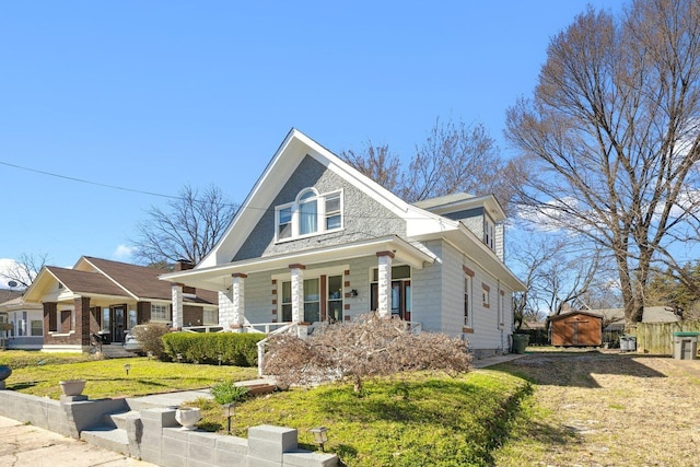 view of front of home featuring covered porch, fence, an outdoor structure, a shed, and a front yard