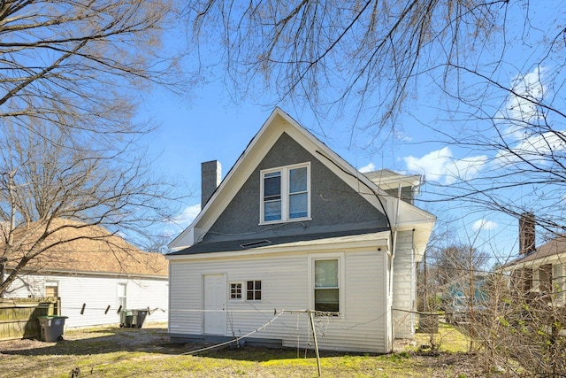 rear view of house featuring a chimney and fence