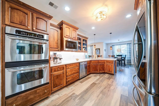 kitchen with visible vents, glass insert cabinets, a peninsula, stainless steel appliances, and light wood-style floors