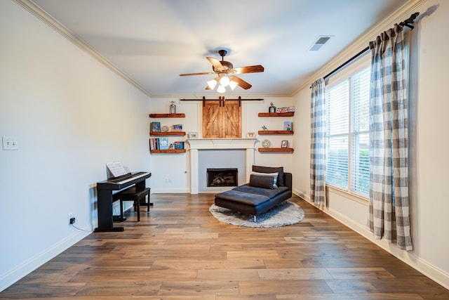 sitting room with a barn door, visible vents, crown molding, and wood finished floors