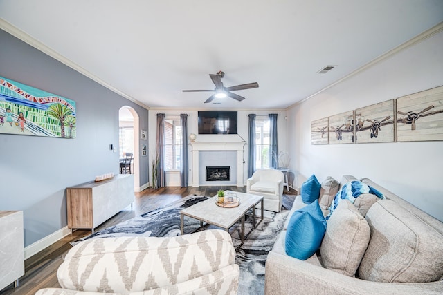 living area with arched walkways, a fireplace, crown molding, and wood finished floors