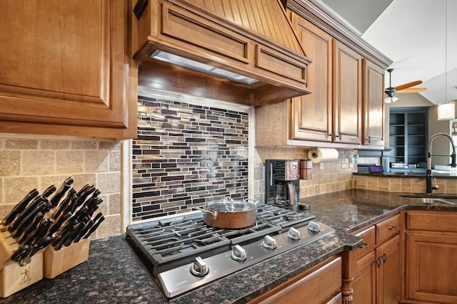 kitchen with premium range hood, a sink, tasteful backsplash, brown cabinetry, and stainless steel gas stovetop