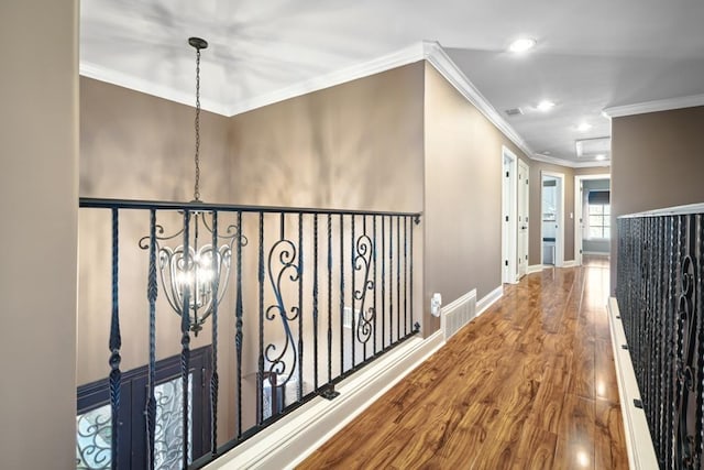 hall featuring baseboards, visible vents, wood finished floors, an inviting chandelier, and crown molding