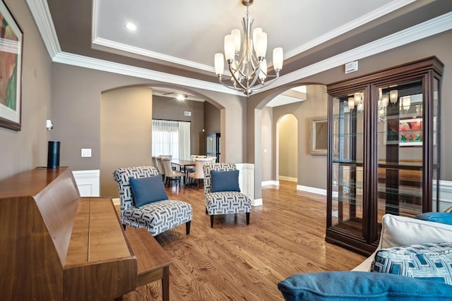 interior space with arched walkways, wood finished floors, ornamental molding, a tray ceiling, and an inviting chandelier