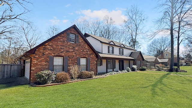 tudor-style house featuring a garage, brick siding, fence, and a front lawn