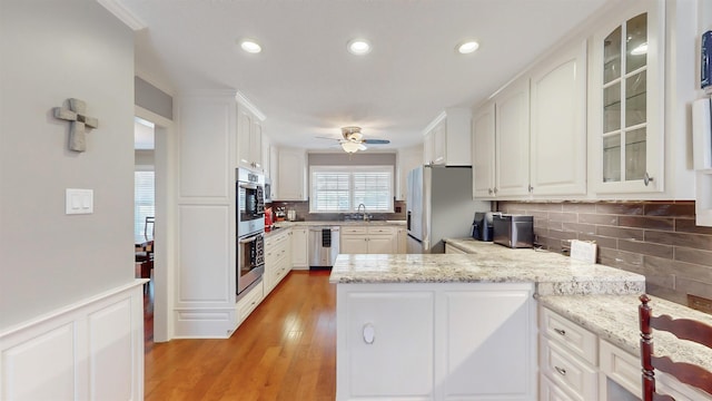 kitchen featuring appliances with stainless steel finishes, a wainscoted wall, white cabinets, and a peninsula