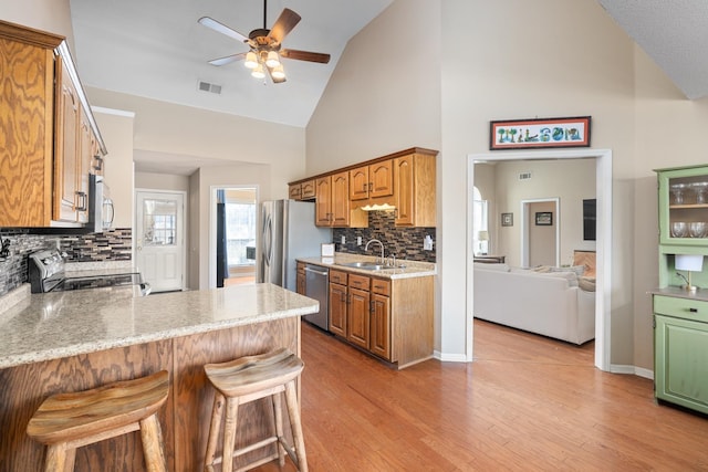 kitchen featuring light wood-style flooring, a peninsula, a sink, a kitchen breakfast bar, and appliances with stainless steel finishes