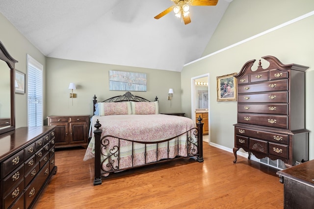 bedroom with a ceiling fan, high vaulted ceiling, ensuite bathroom, and wood finished floors