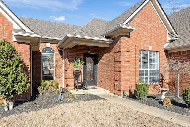 doorway to property with a shingled roof and brick siding