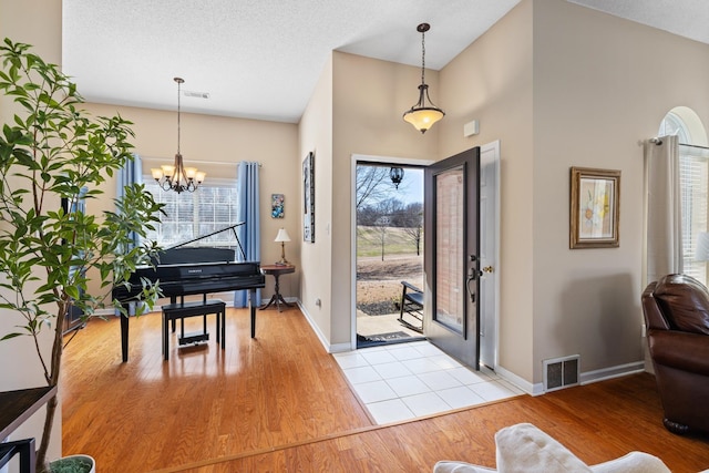 entrance foyer featuring visible vents, a textured ceiling, light wood finished floors, and an inviting chandelier