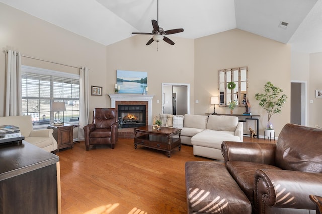 living area featuring visible vents, a ceiling fan, light wood-type flooring, a fireplace, and high vaulted ceiling