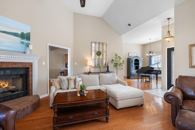 living area featuring a brick fireplace, visible vents, an inviting chandelier, and wood finished floors