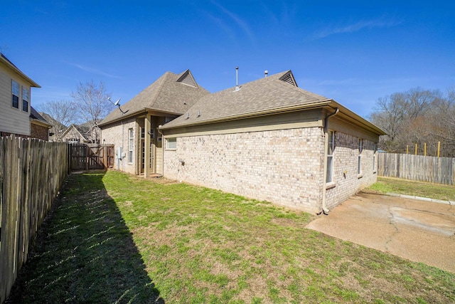 back of property with a shingled roof, brick siding, a yard, and a fenced backyard