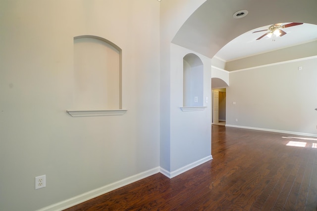 empty room featuring a ceiling fan, arched walkways, baseboards, and wood finished floors