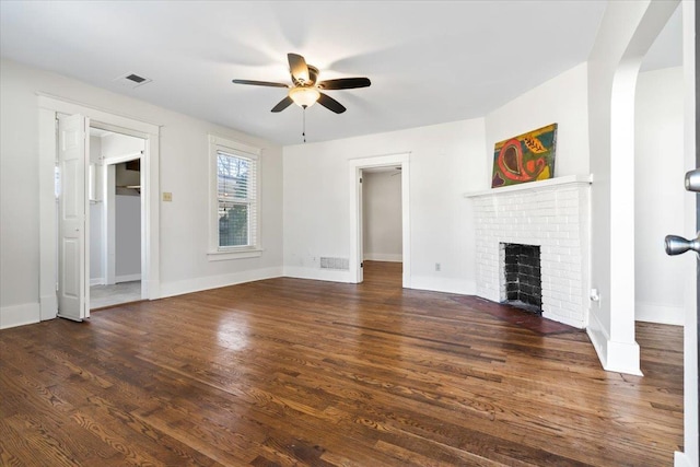 unfurnished living room with visible vents, baseboards, dark wood-style floors, ceiling fan, and a brick fireplace