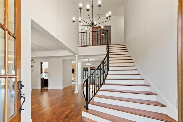 staircase with ornamental molding, baseboards, an inviting chandelier, and wood finished floors