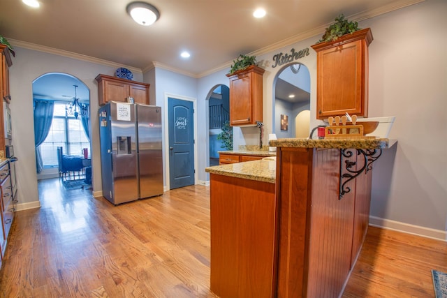 kitchen featuring arched walkways, brown cabinetry, crown molding, light wood-style floors, and stainless steel refrigerator with ice dispenser