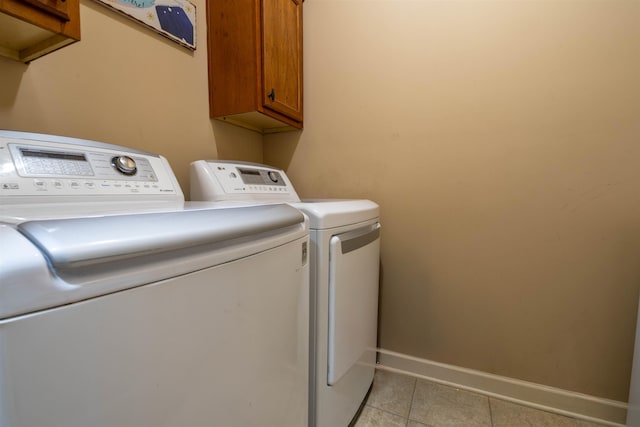 washroom with cabinet space, baseboards, light tile patterned flooring, and washing machine and clothes dryer