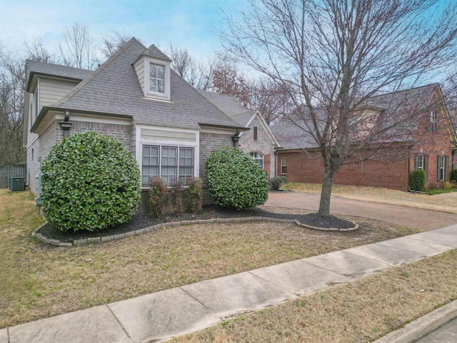 view of front of home featuring central AC, brick siding, a front lawn, and a shingled roof