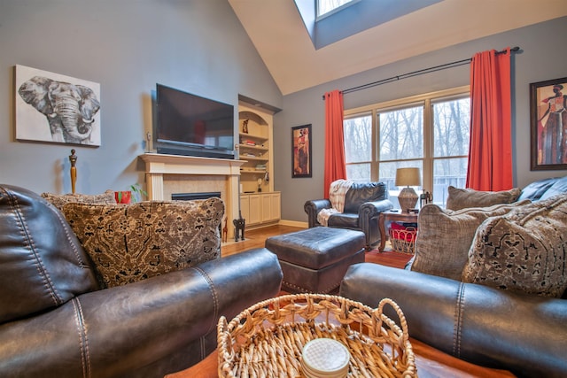 living room featuring built in shelves, a skylight, a fireplace, wood finished floors, and high vaulted ceiling