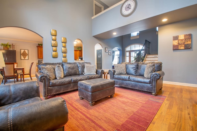 living area featuring arched walkways, stairway, wood finished floors, and baseboards