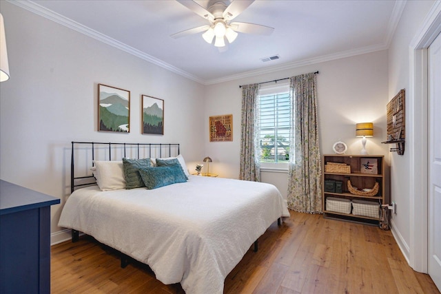 bedroom featuring ceiling fan, visible vents, baseboards, wood-type flooring, and crown molding