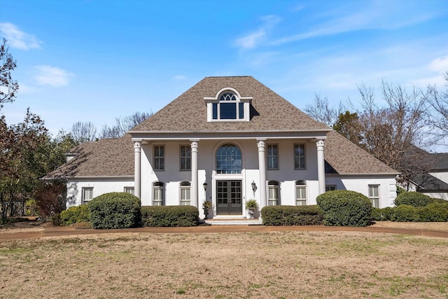 greek revival inspired property featuring stucco siding, a front lawn, french doors, and roof with shingles