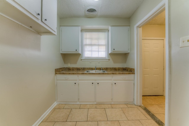 kitchen featuring visible vents, white cabinets, a sink, a textured ceiling, and baseboards