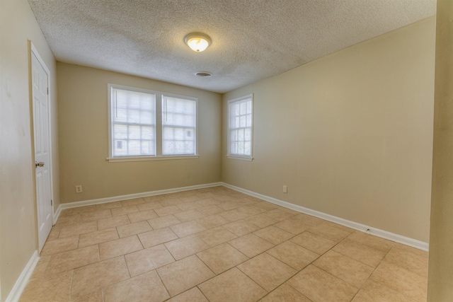 spare room with light tile patterned floors, baseboards, and a textured ceiling