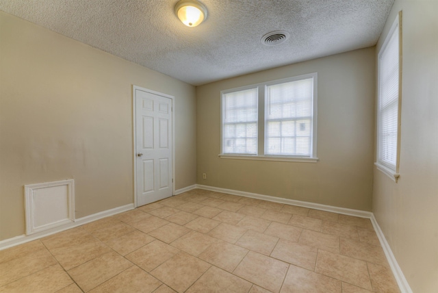 spare room featuring visible vents, a textured ceiling, baseboards, and light tile patterned flooring